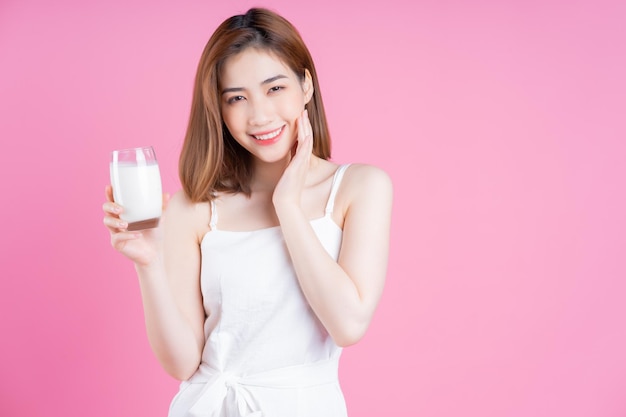 Image of young Asian woman drinking milk on pink background