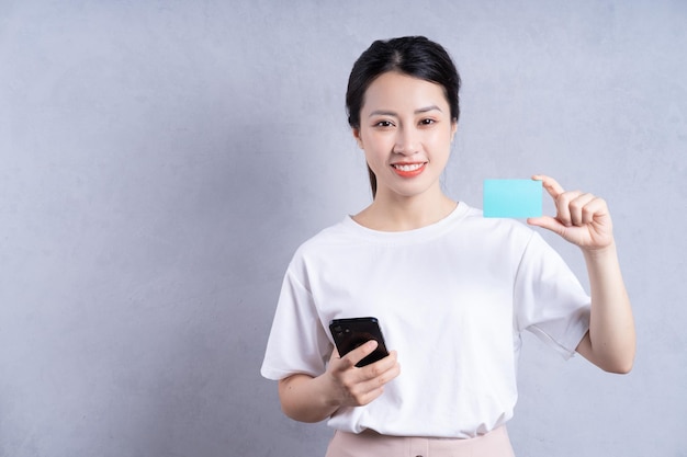 Image of young Asian woman holding bank card on background