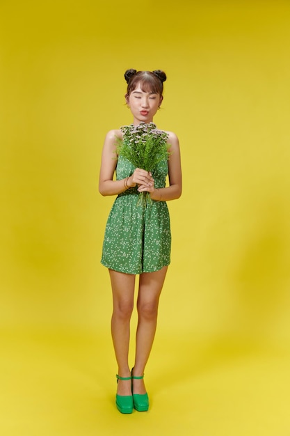 Image of young asian woman holding flowers on yellow background