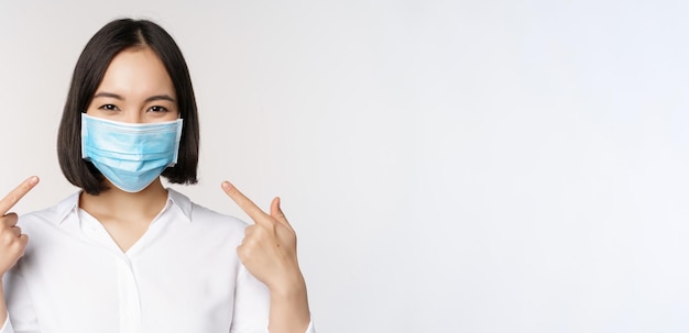 Image of young asian woman pointing at herself while wearing medical face mask concept of covid prot