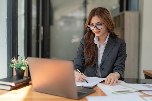 Image of a young beautiful brooding Asian woman working with a laptop while sitting at a laptop in the office thinking of a professional plan project management and considering new business ideas