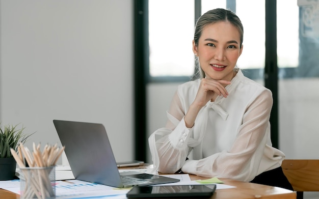 オフィスでラップトップで作業しながら笑っている若い美しいうれしそうな女性の画像