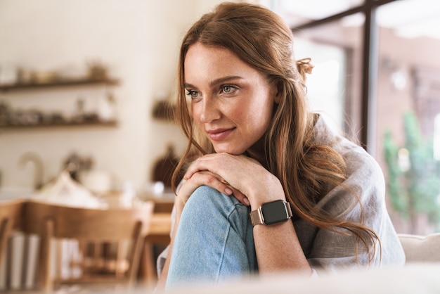 Image of young beautiful redhead woman indoors sitting at the kitchen at home.