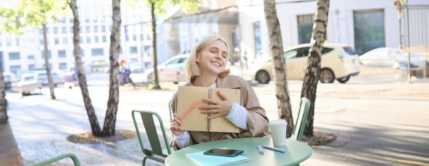 Foto immagine di una giovane bellissima studentessa che fa i compiti in un caffè all'aperto con un giornale in mano o