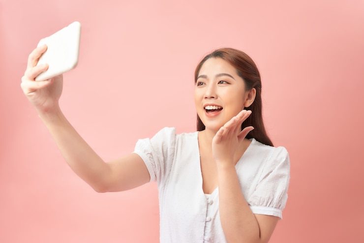 Photo 웃 고 핑크 이상 격리 핸드폰에 셀카 사진을 복용 긴 머리를 가진 젊은 갈색 머리 아시아 여자의 이미지