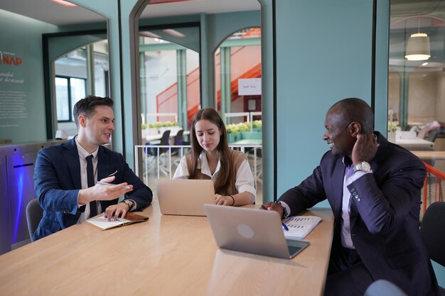 Image of young businessmen and colleague discussing document in laptop and touchpad at meeting