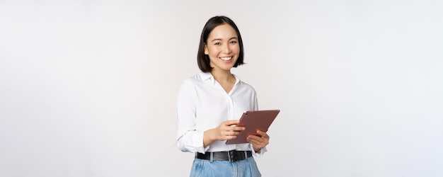Изображение молодого генерального директора корейской работающей женщины, держащей планшет и улыбающейся, стоящей на белом фоне