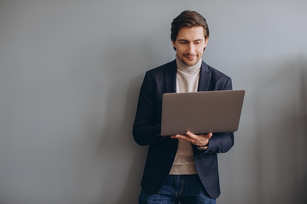 Image of young cheerful businessman in suit holding and using laptop in the modern office