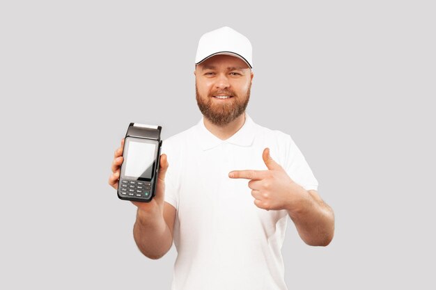 Image of young cheerful delivery man pointing at POS terminal for paying with credit card