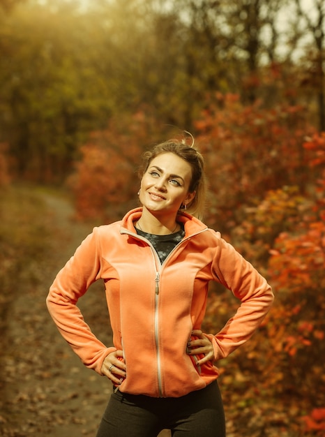 木の上に赤みを帯びた葉を持つ秋の森のスポーツウェアの若いフィット女性の画像