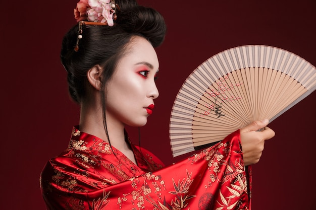 Image of young geisha woman in traditional japanese kimono holding wooden hand fan
