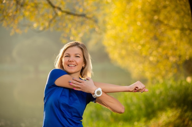 Image of young girl stretching in summer park in afternoon