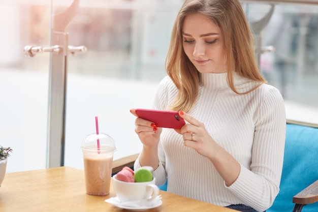 Image of young good looking blonde female sits in cafe