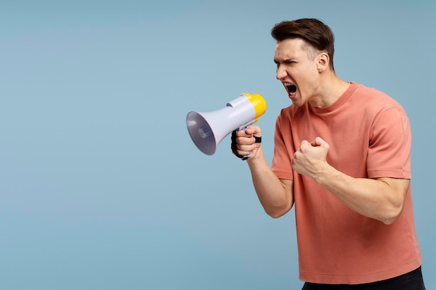 Image of young handsome man standing over blue background and screaming with mouthpiece