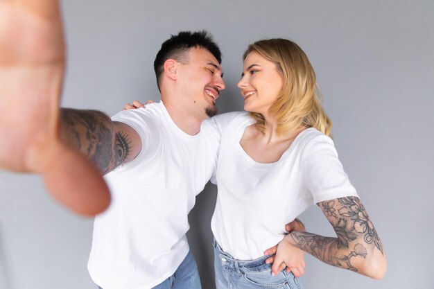 Image of young happy man kissing and hugging beautiful woman while taking selfie photo on gray wall