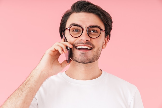 Изображение молодого радостного человека в очках разговаривает по мобильному телефону и улыбается изолированно