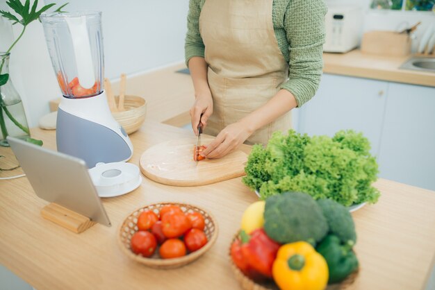Изображение молодой леди, стоящей на кухне с помощью планшетного компьютера и готовящей овощной салат