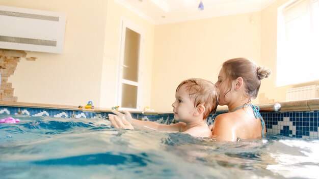 彼女の小さな3歳の男の子の子供を泳ぐことを教え、屋内プールでカラフルなビーチボールで遊ぶ若い母親の画像