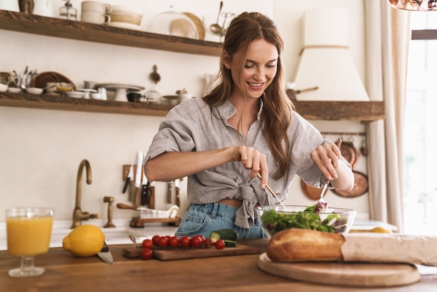 Image of young pleased happy concentrated cute beautiful woman indoors at the kitchen cooking.