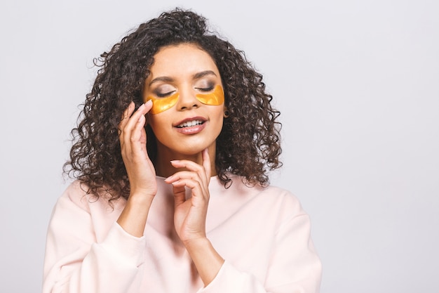 Image of young pure beautiful afro american woman standing naked isolated against white take care of her skin with under eye patches.