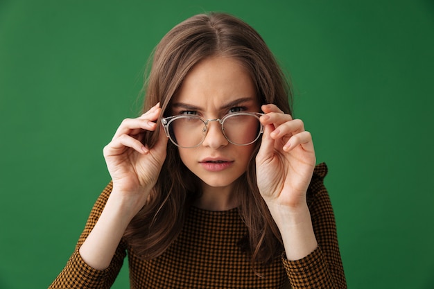 Image of young serious woman standing isolated over green wall wearing glasses 