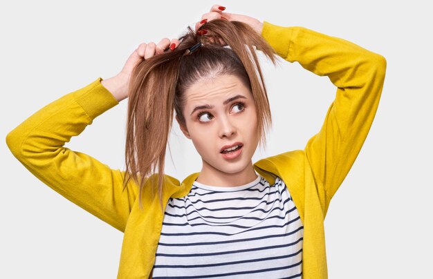 Image of young woman collecting hair in a ponytail wearing casual outfit posing over white studio wall Female makes ponytail advertises healthy natural hair and looks up to copy space