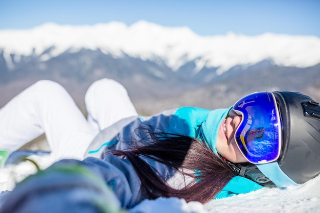 Image of young woman in helmet and with snowboard lying on mountain slope