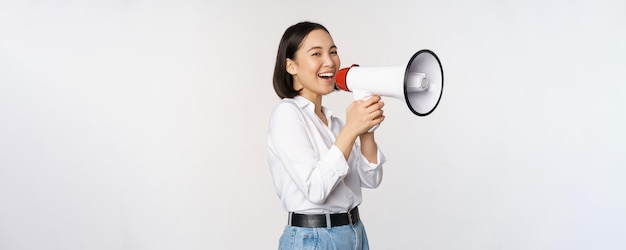 Image of young woman korean activist recruiter screaming in megaphone searching shouting at loudspeaker standing over white background