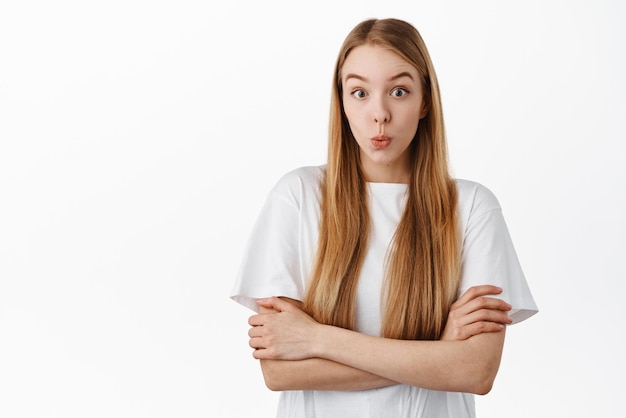 Image of young woman in tshirt cross arms on chest and looks surprised say wow stare with curious and excited face checking out something cool standing over white background