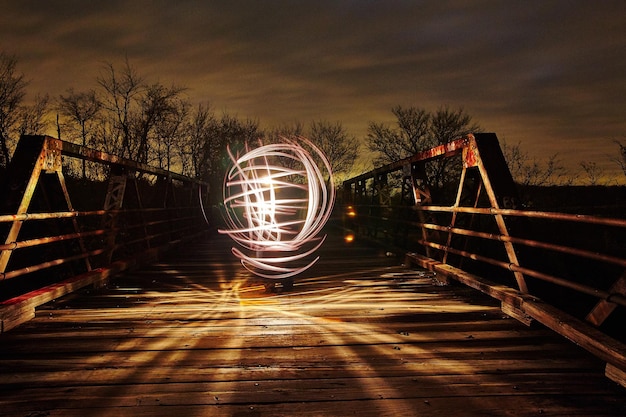 Image of Zigzagging white light lights up a metal bridge at dusk