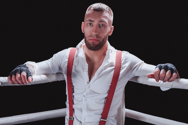 Foto immagini di un uomo barbuto in camicia bianca e bretelle rosse sul ring. il concetto di pugni combattimenti sotterranei. tecnica mista