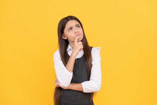 Imaginative girl child in school uniform keep thinking yellow background, imagination.