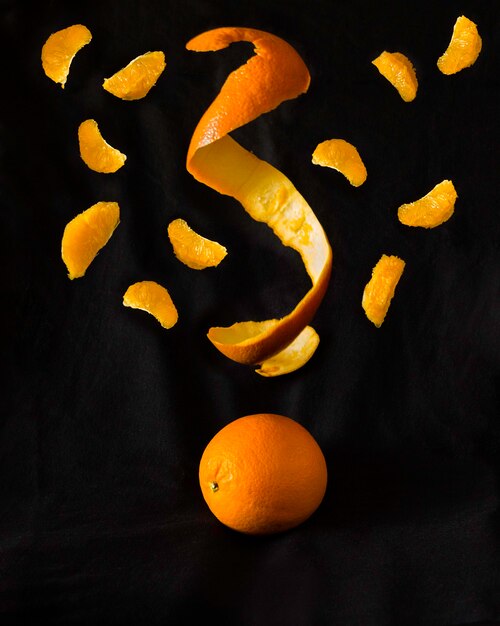 Foto fantasiosa di arancione su nero con i segmenti e la pelle che cadono. concetto di cibo divertente. copia spazio.