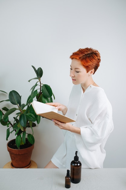 Immersed short-haired woman looking at the eco-friendly notebook with a carton cover. She is turning blak pages, pretending to read it.