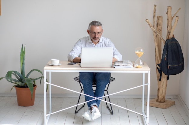 Photo immersion in work. focused gray-haired man in glasses looking intently at laptop while sitting working at table in office