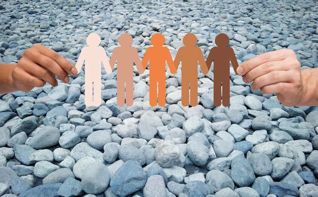 Photo immigration, unity, population, race and humanity concept - multiracial couple hands holding chain of paper people pictogram over stones in desert background