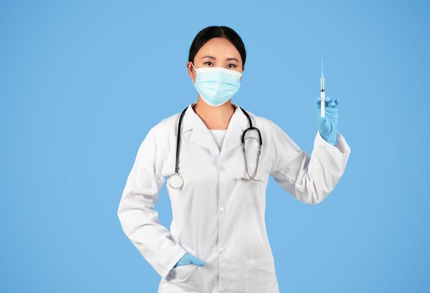 Immunisatieconcept zelfverzekerde aziatische vrouwelijke arts die een beschermend medisch masker draagt met een spuit