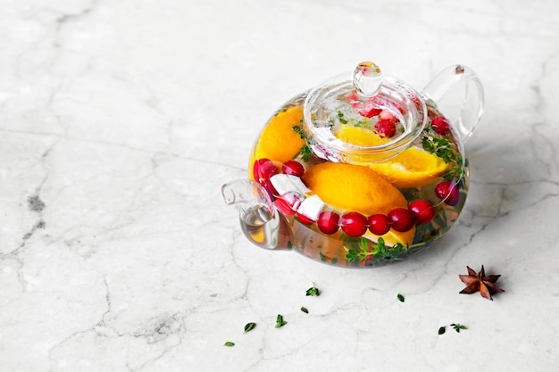 Immunity boosting drink Thyme Tea with cranberries orange and spices in glass teapot on marble table