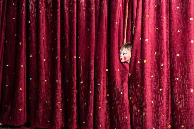 Impatient little boy on stage poking his head out from between the closed curtains as he looks to see what the delay is for the start of the play or pantomime