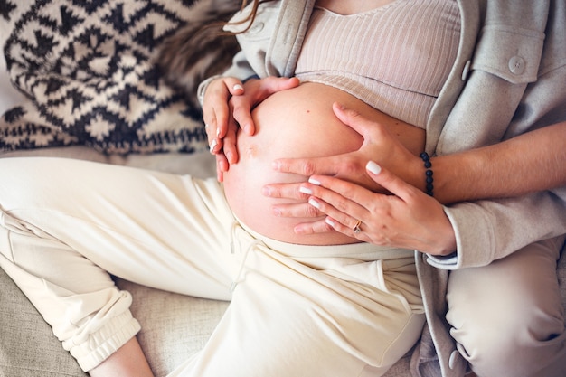 An impersonal young couple waiting for the baby sit and hold their hands on their moms stomach conce...