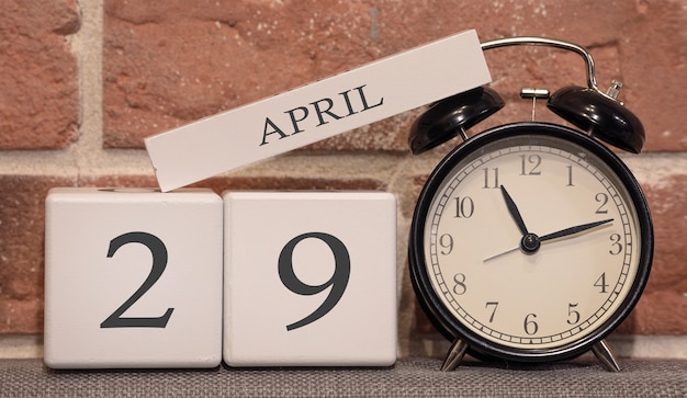 Важная дата, 29 апреля, весенний сезон. Календарь из дерева на фоне кирпичной стены. Ретро будильник как концепция управления временем.