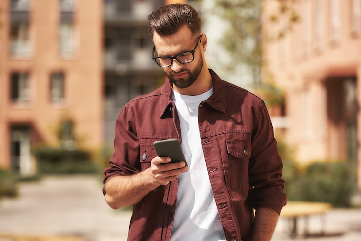 Photo important message serious bearded man in casual wear and eyeglasses looking at his smartphone while