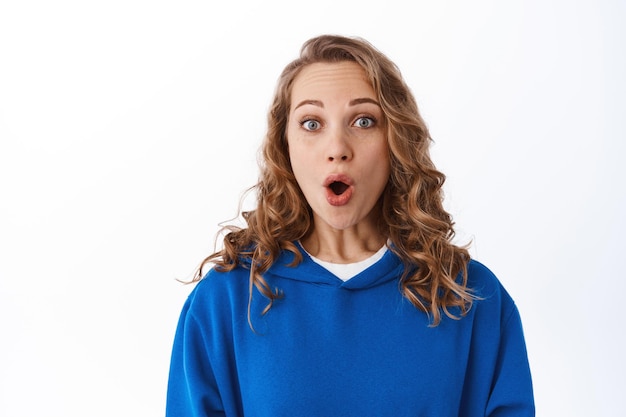 Impressed blond woman gasping fascinated, staring excited and say wow, checking out something cool, standing astounded against white background