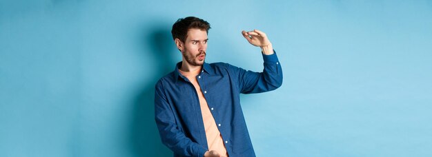 Impressed caucasian guy staring at empty space with big object shaping large size standing on blue b