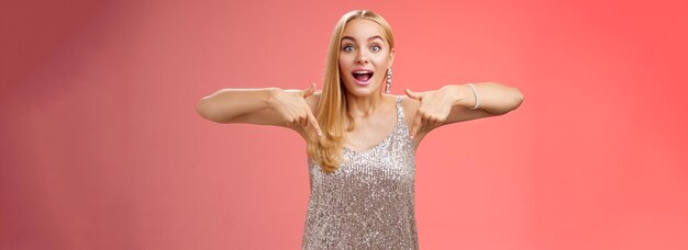 Photo impressed excited attractive glamour blond girl in silver glittering dress gasping thrilled pointing