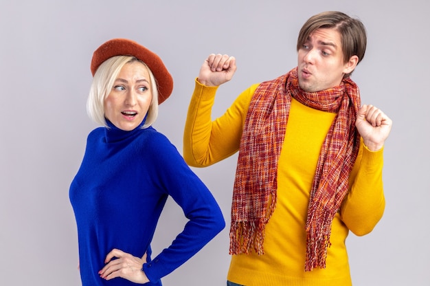 Impressed handsome slavic man with scarf around his neck standing with raised fists and looking at pretty blonde woman with beret