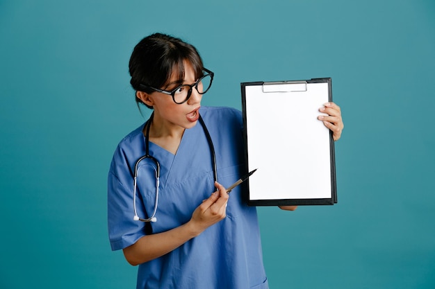 Photo impressed holding clipboard young female doctor wearing uniform fith stethoscope isolated on blue background