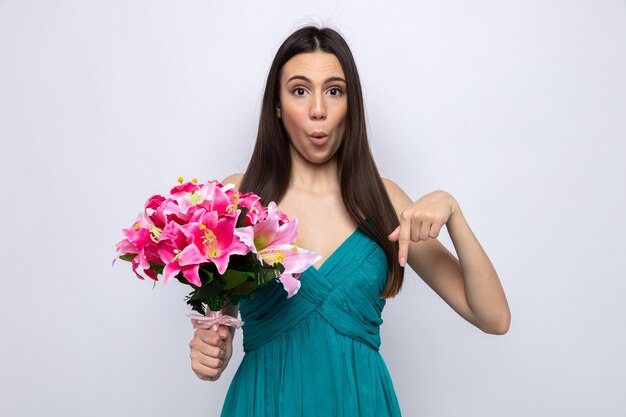 Impressed points at down beautiful young girl holding bouquet isolated on white wall