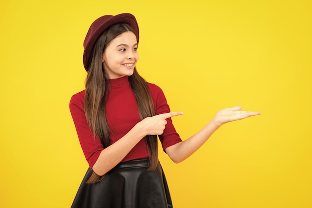 Impressed teenage girl showing recommendation copyspace Child teenager points away pointing aside at copy space Happy teenager portrait Smiling girl