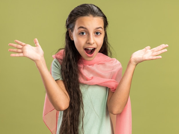 Adolescente impressionato che indossa uno scialle guardando la parte anteriore che mostra le mani vuote isolate sul muro verde oliva